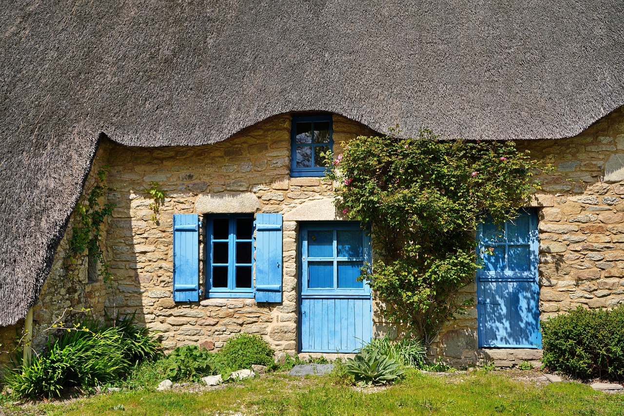 Chaumière en pierre aux portes et volets bleus, rosier grimpant sur la façade
