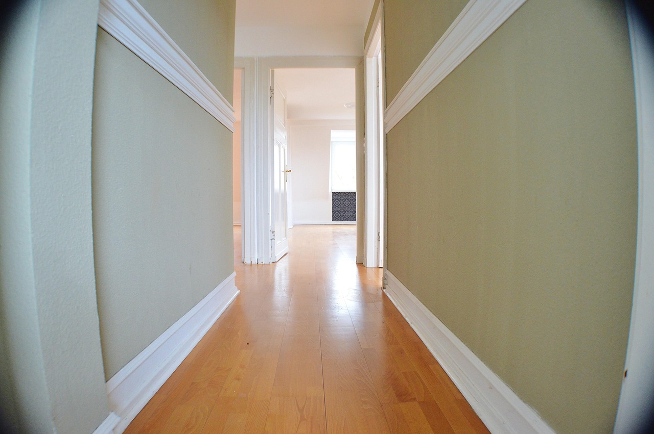 Hallway of an empty flat with light wooden flooring, doors open onto a cleared room