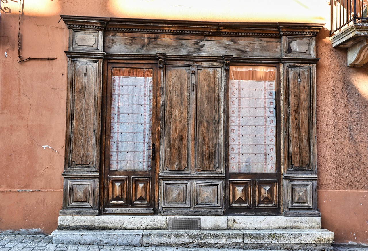 Devanture en bois d'un ancien commerce fermé, rideaux aux vitrines, sur une façade enduite