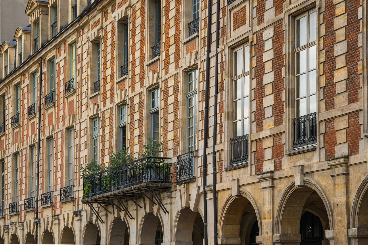 Façade d'immeuble ancien en brique et pierre, avec des balcons en fer forgé au-dessus d'arcades