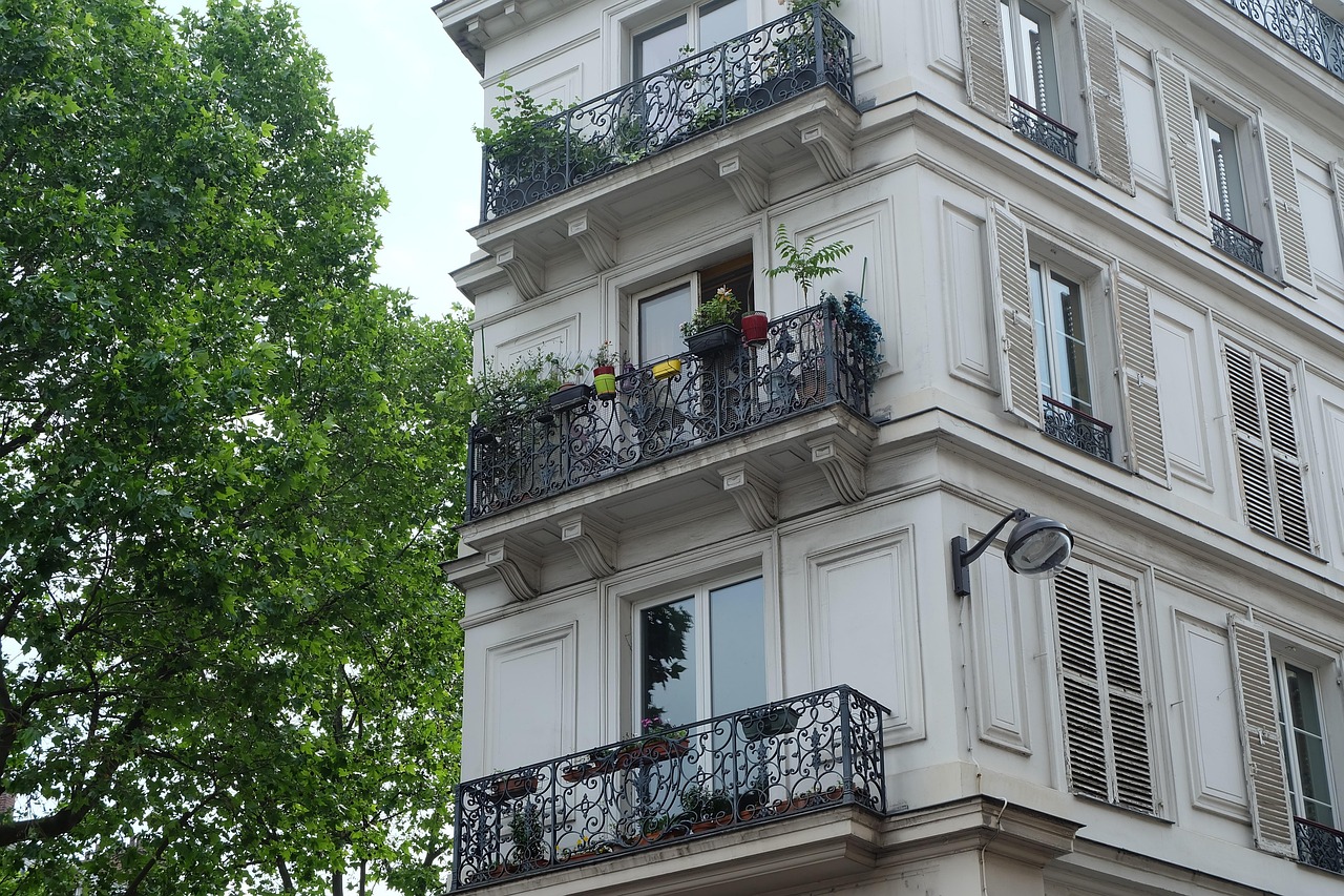 Angle d'un immeuble d'habitation ancien à balcons en fer forgé et volets persiennés, à côté d'un platane