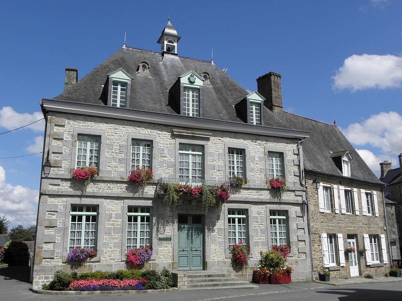 Façade en granit d'une mairie de village aux fenêtres fleuries