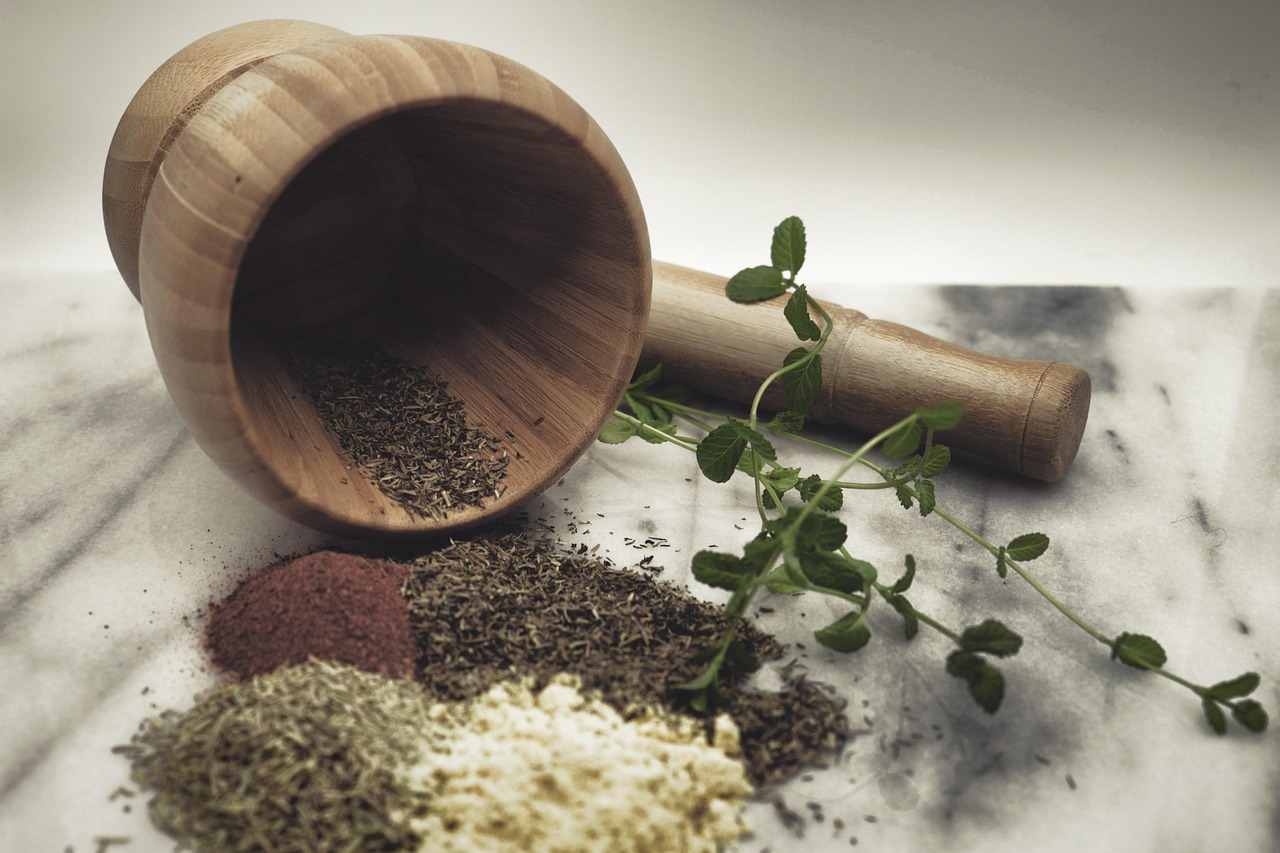 Wooden mortar and pestle with dried herbs on a marble worktop