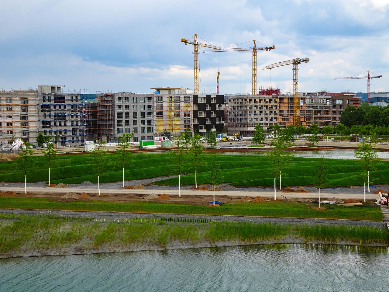 quartier neuf en construction, grues et parc paysager en cours d'aménagement au bord d'un plan d'eau