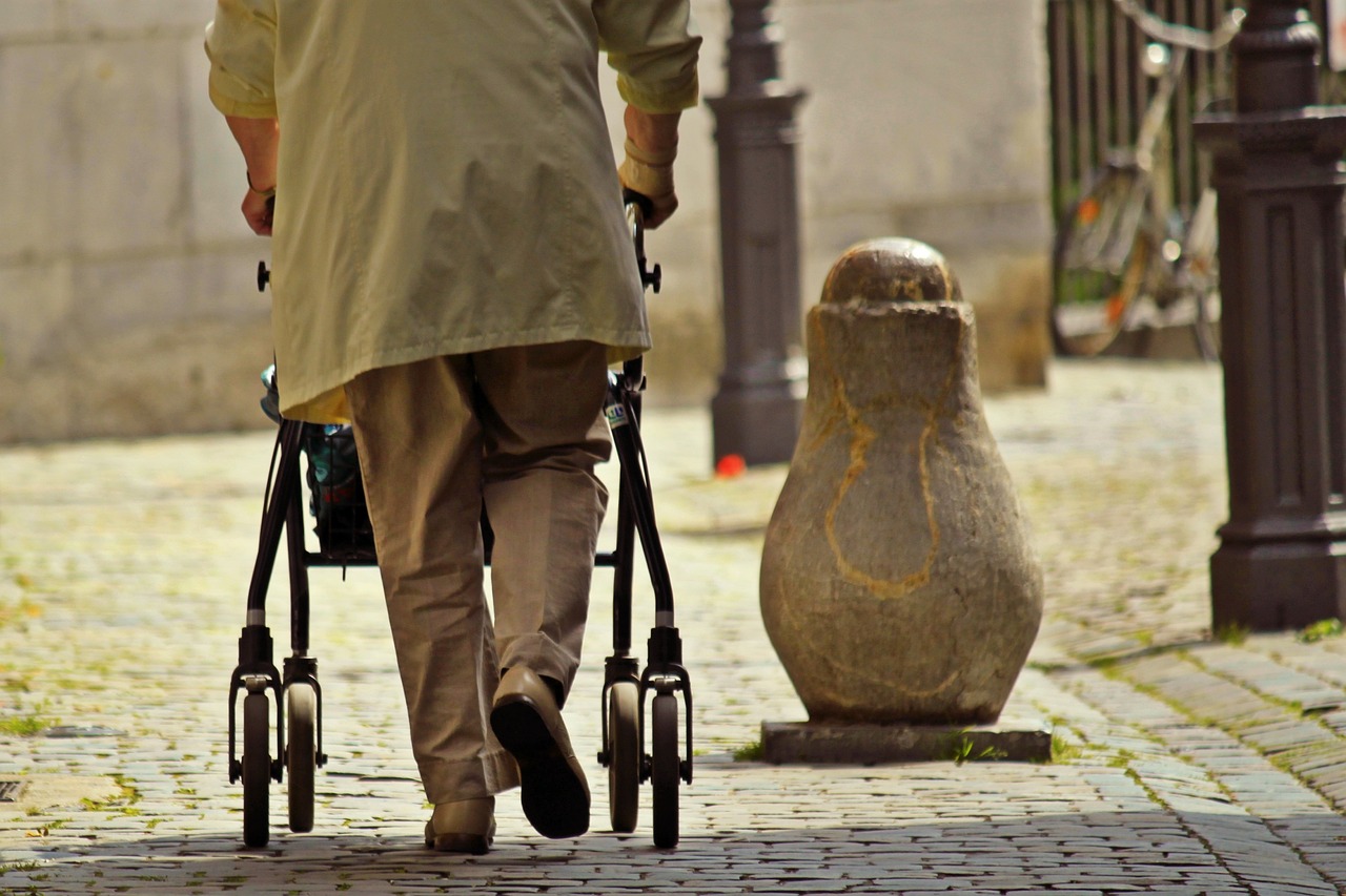 Elderly person seen from behind walking with a rollator along a cobbled street