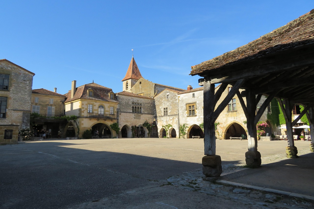 Place de bastide bordée de maisons à arcades et de rez-de-chaussée commerçants, vue depuis la halle couverte