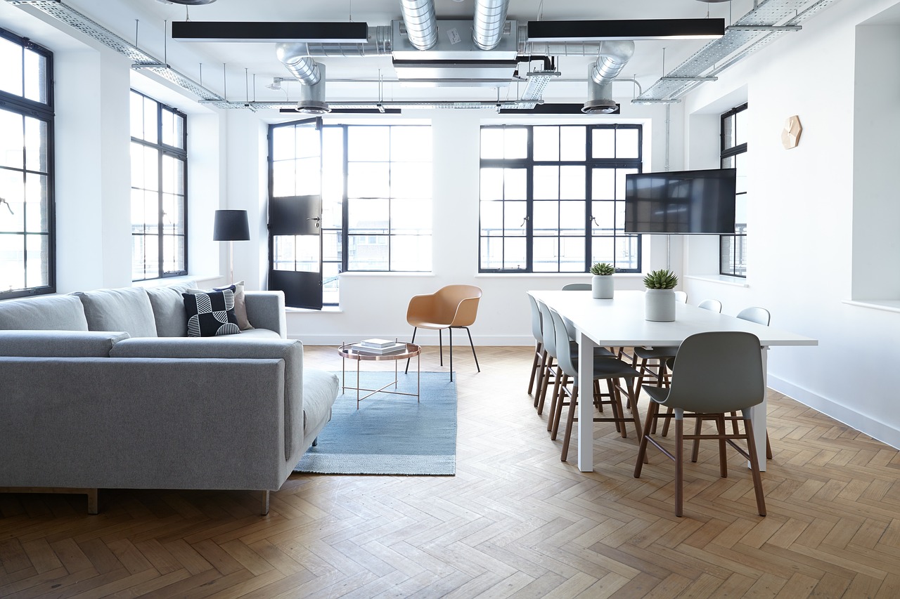 Bright, unoccupied office floor with large windows, herringbone parquet, a sofa and a meeting table
