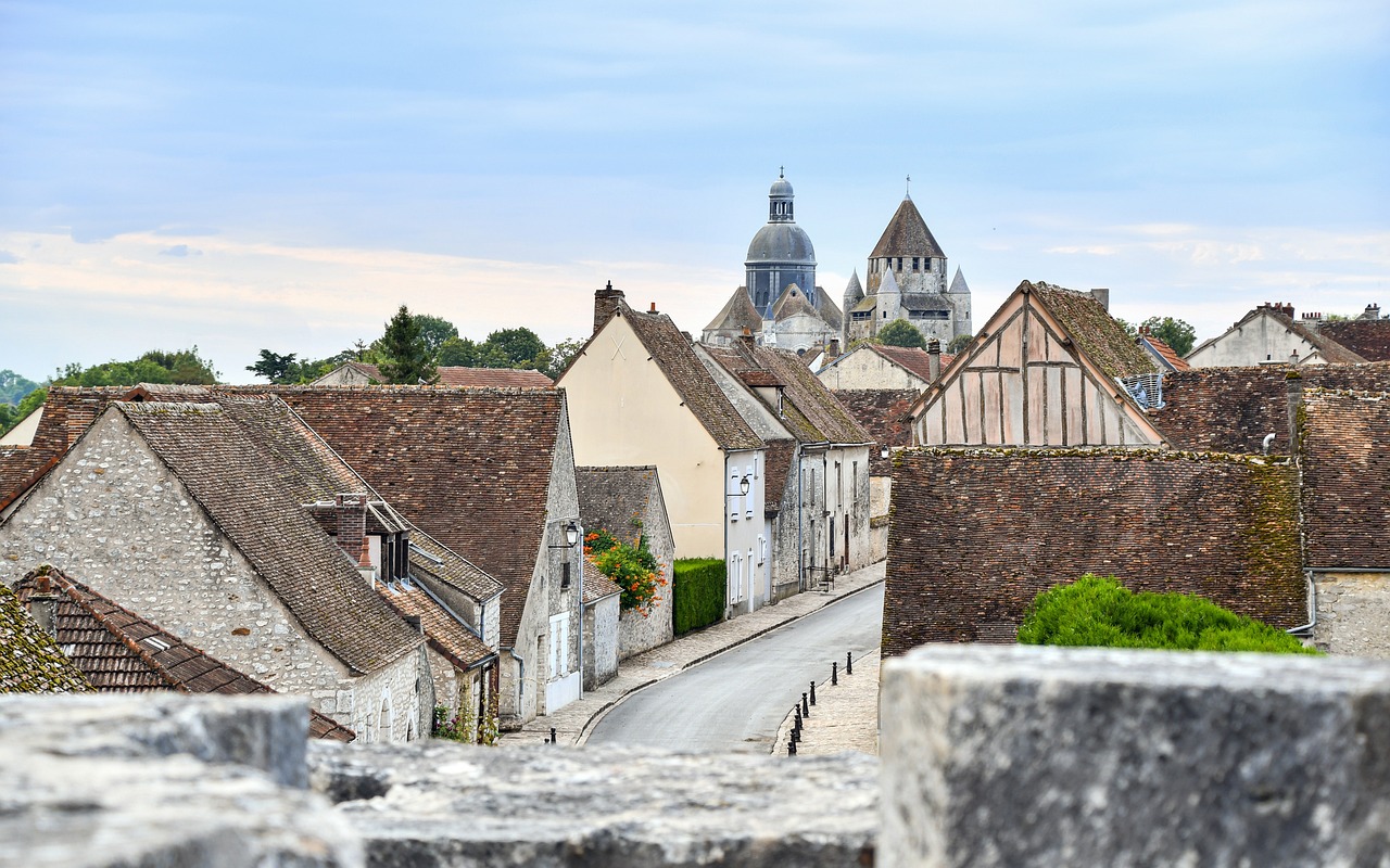 rue en pente bordée de maisons anciennes à toits de tuiles, avec le dôme d'une collégiale et un donjon médiéval à l'arrière-plan