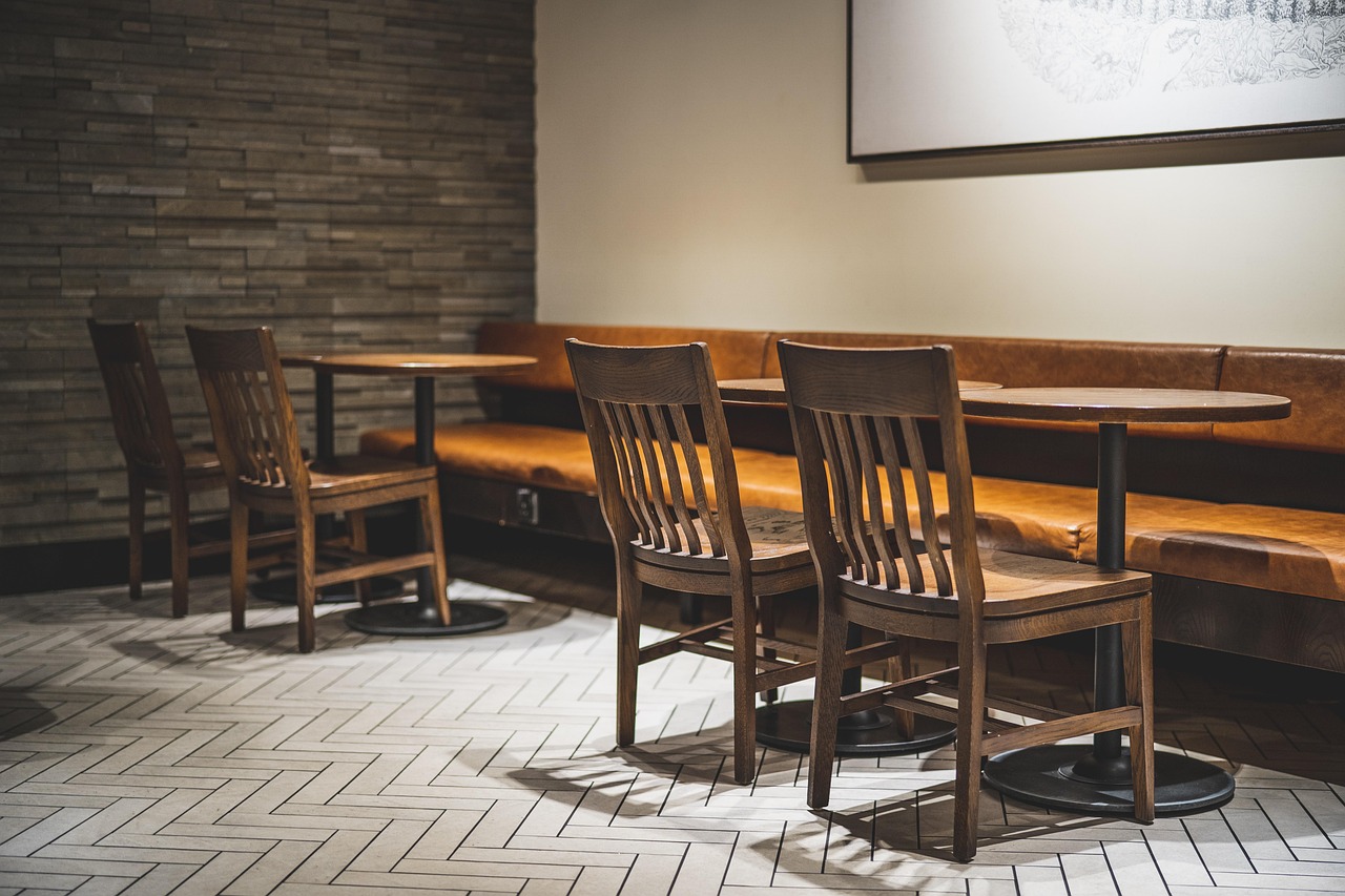 Salle de restaurant vide : tables rondes, chaises en bois et banquette en cuir le long du mur