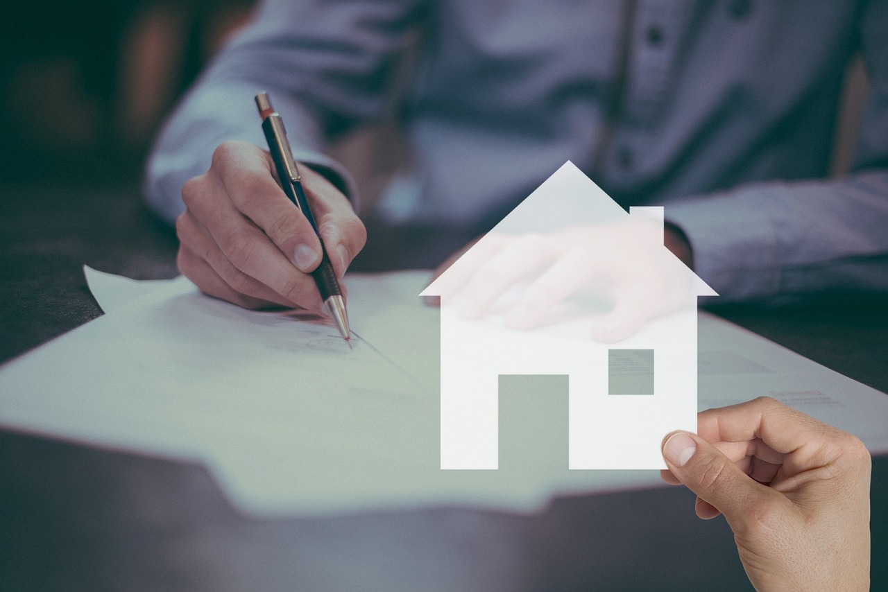 Signing a contract, with a paper house cut-out in the foreground